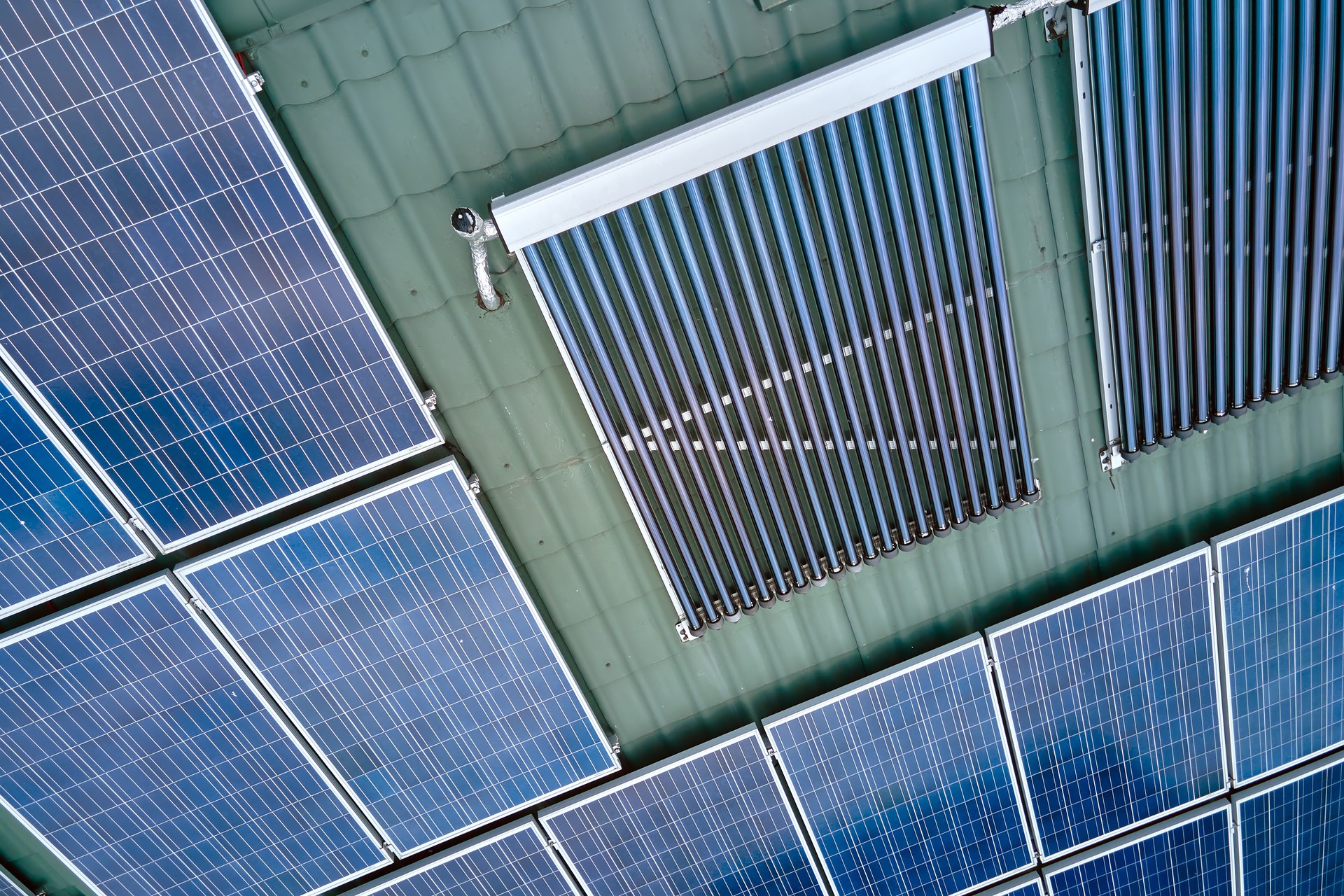 Building roof with rows of blue photovoltaic panels and vacuum air solar collectors for water heating and producing clean ecological electricity. Renewable electric and heat energy with zero emission